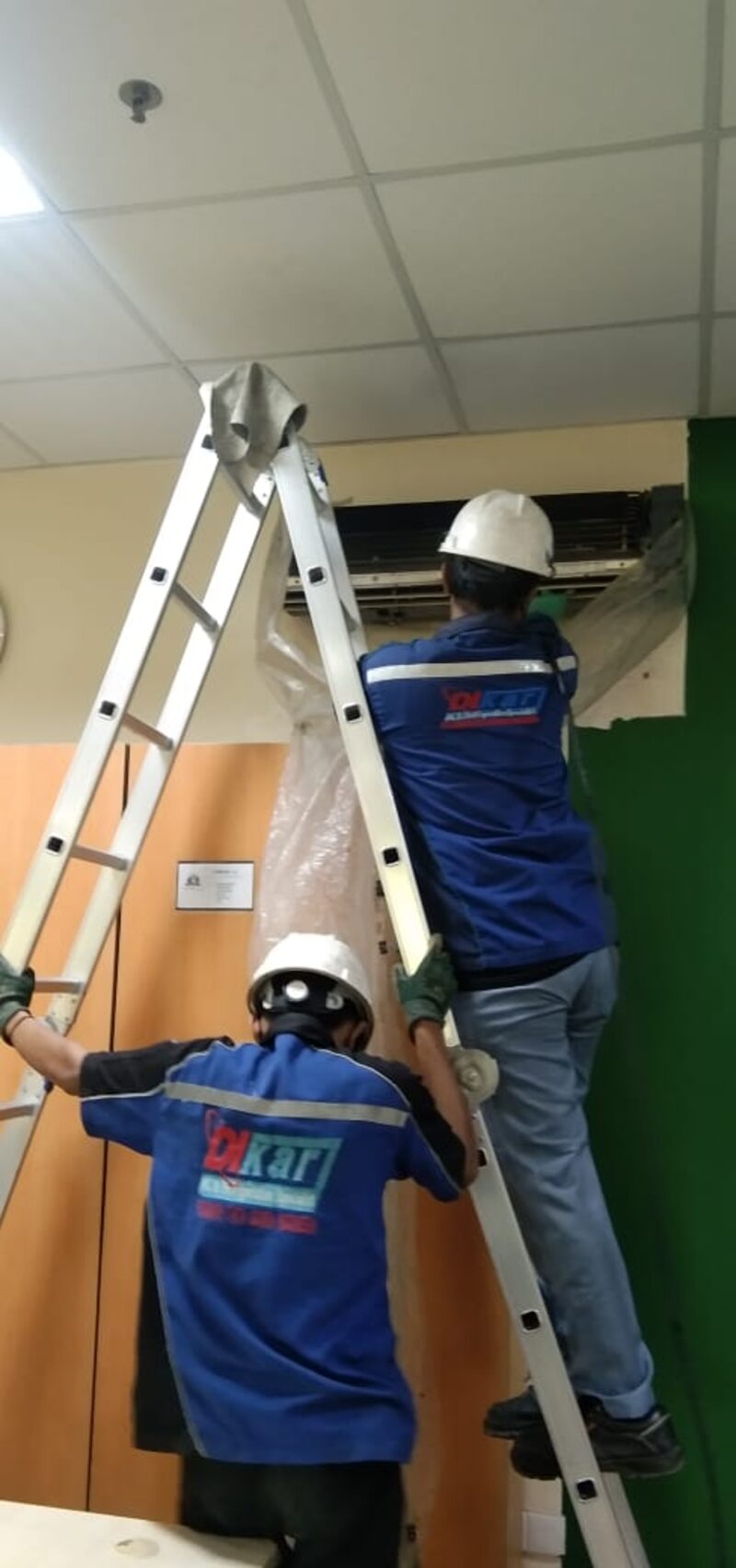 Dua teknisi PT Dikari memasang dan merawat AC Split Duct pada ketinggian